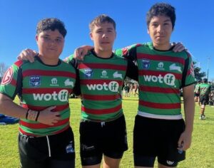 Three players arms around shoulders posing for a picture in their club colours outdoors on a grass field